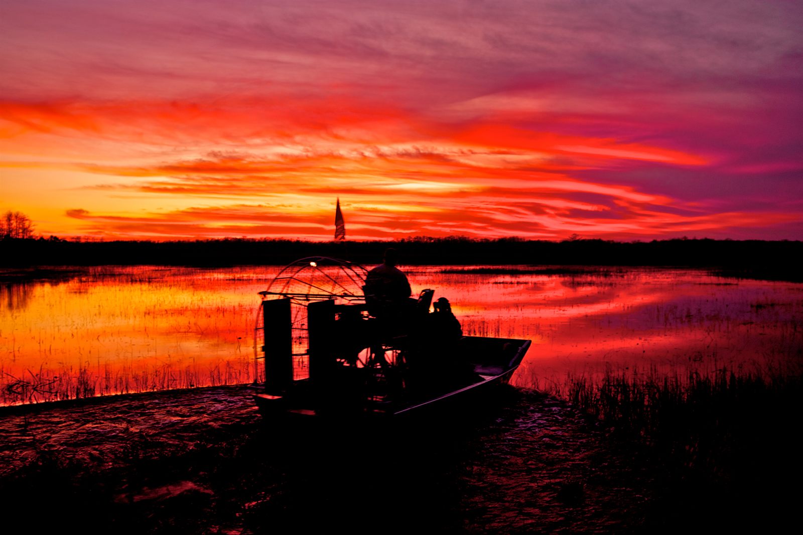 An airboat silhouetted on marsh water under a deep red Florida sunset